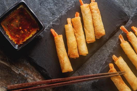 unos rollitos rellenos de langostino y puerro con salsa dulce sobre una tabla de pizarra