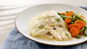 Plato de pescado blanco al vapor con salsa ligera y verduras blandas sobre una mesa clara